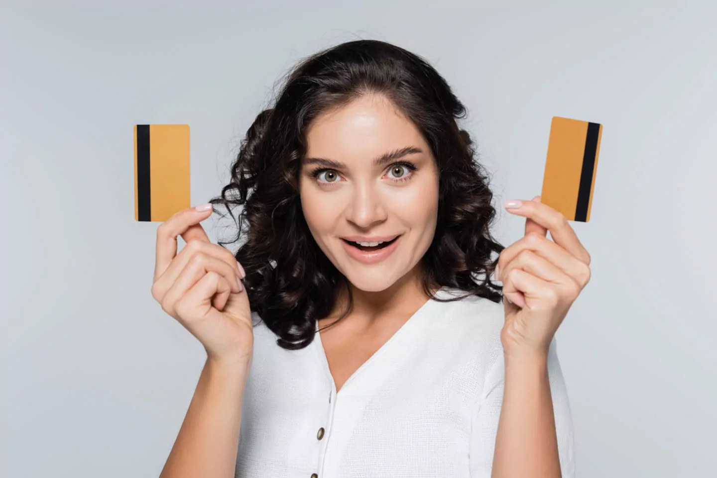amazed young woman holding credit cards with cashback isolated on grey